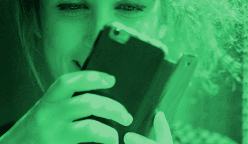 Kvinna använder mobilen i grönt ljus.