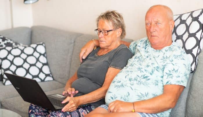 Äldre par sitter i soffan med en laptop.