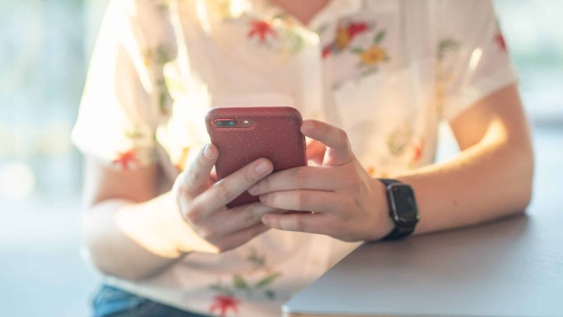 Kvinna sittandes med mobil i handen.