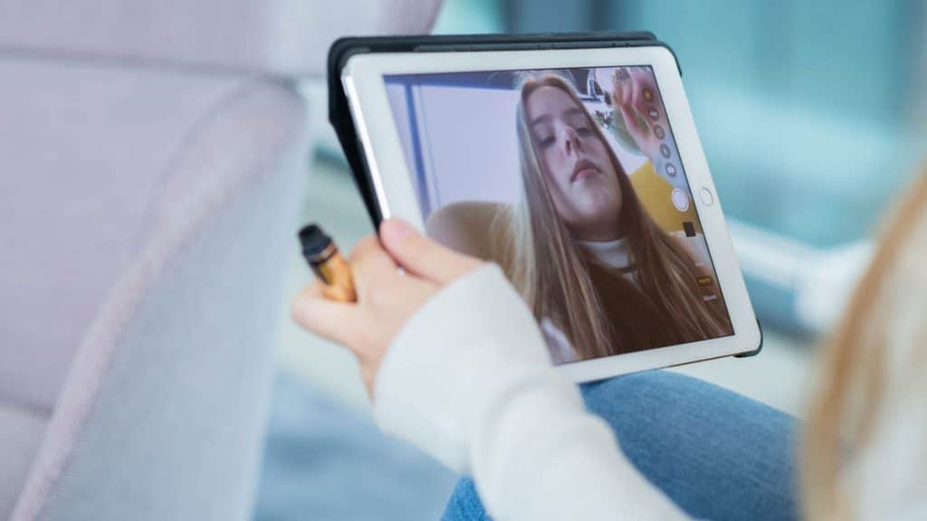 Tonåring speglar sig i iPad medan hon sminkar sig.