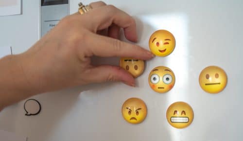 Emojis med olika uttryck sitter på kylskåp. Hand håller en av emojisarna.