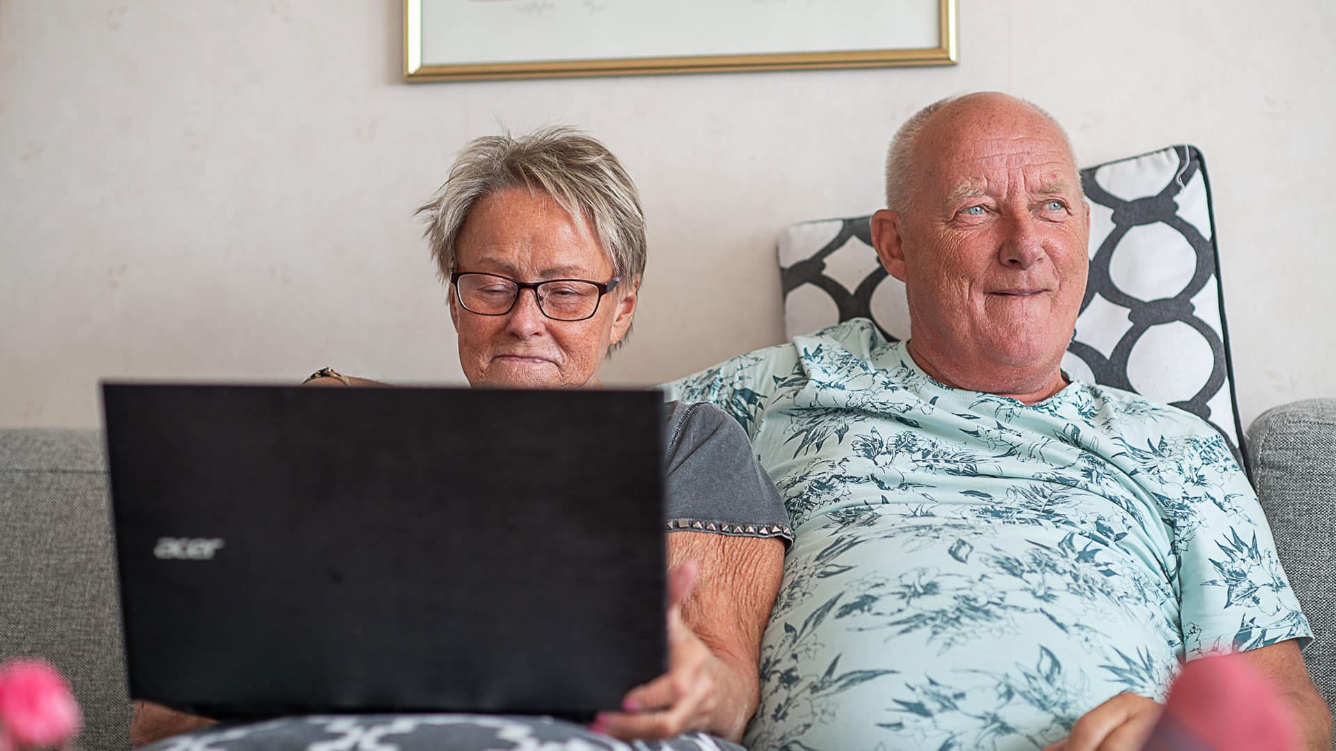 Äldre par som sitter framför bärbar datorn i soffan