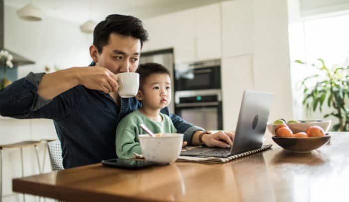 Father multi-tasking with young son (2 yrs) at kitchen table