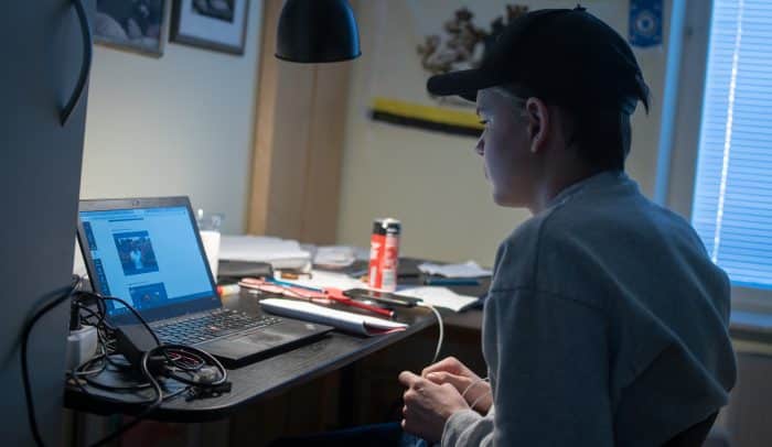 En kille med keps sitter framför sin dator vid ett skrivbord i sitt rum hemma och studerar