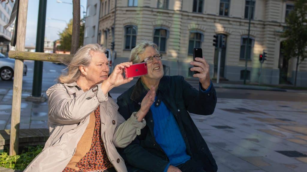 Äldre par som tittar på sina mobiler ute på ett torg