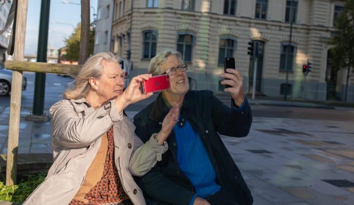 Äldre par som tittar på sina mobiler ute på ett torg