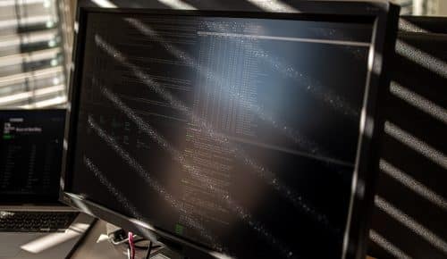En dammig dataskärm med kod blir beslyst av solstrålar genom ett fönster med persienner på ett kontor.