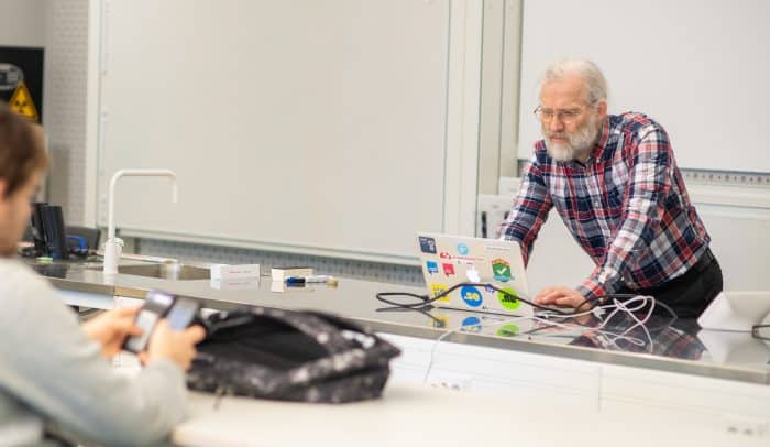 En föreläsningssal på på KTH. En föreläsare tittar på sin dator medan en student tittar på sin telefon vid ett bord.