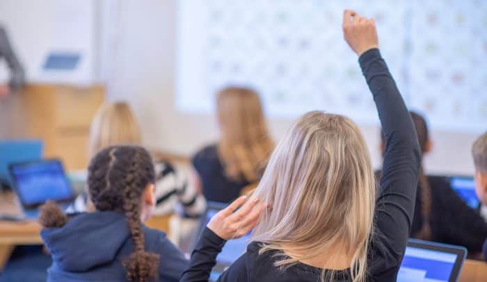 Elev i klassrum räcker upp handen.