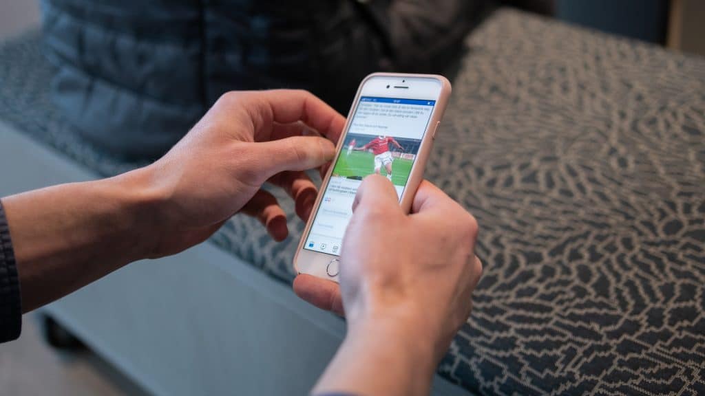 Händer som scrollar på en mobil, en influencer i form av en fotbollsspelare syns på skärmen.