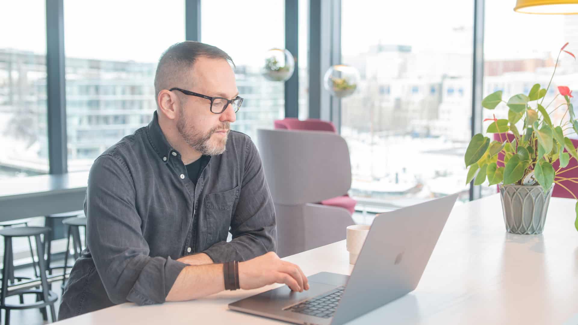 En man jobbar på en bärbar dator stående vid ett bord bredvid en krukväxt