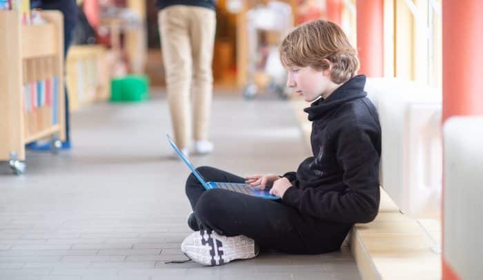Elev i mellanstadieålder sitter på golvet i skolmiljö och använder en dator.