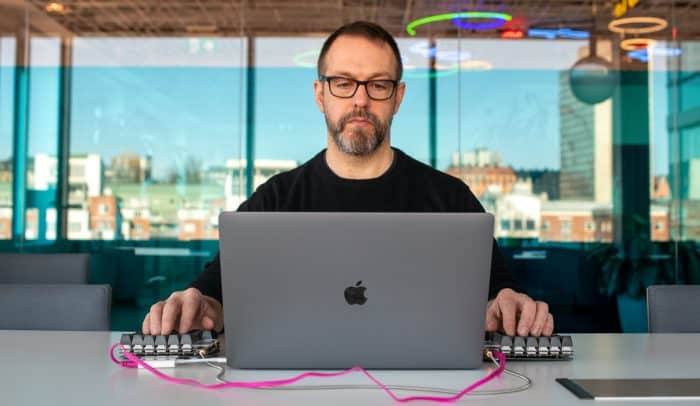 En man sitter vid en dator med ett mindre tangentbord på varje sida och jobbar med DNS