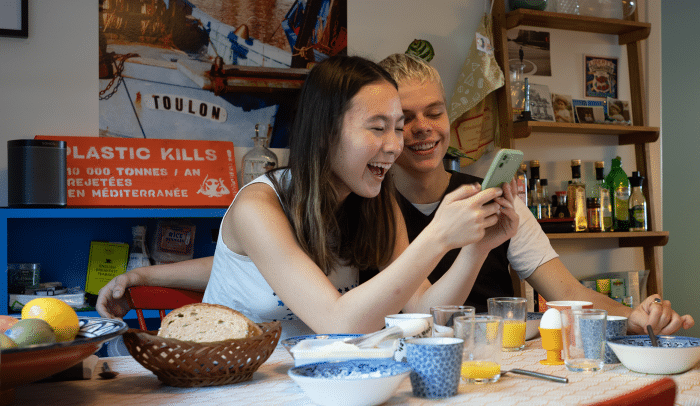 Två unga som sitter vid frukostbordet och tittar på en mobiltelefon