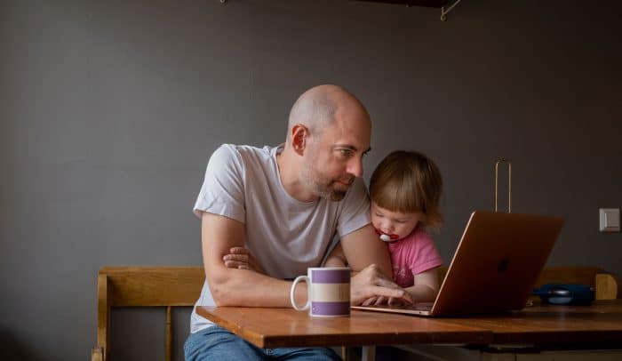 En pappa och hans son sitter tillsammans vid ett köksbord med en dator och kaffekopp framför sig