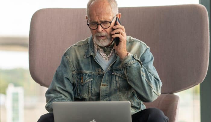 Äldre man sitter framför datorn och ringet ett telefonsamtal, orolig