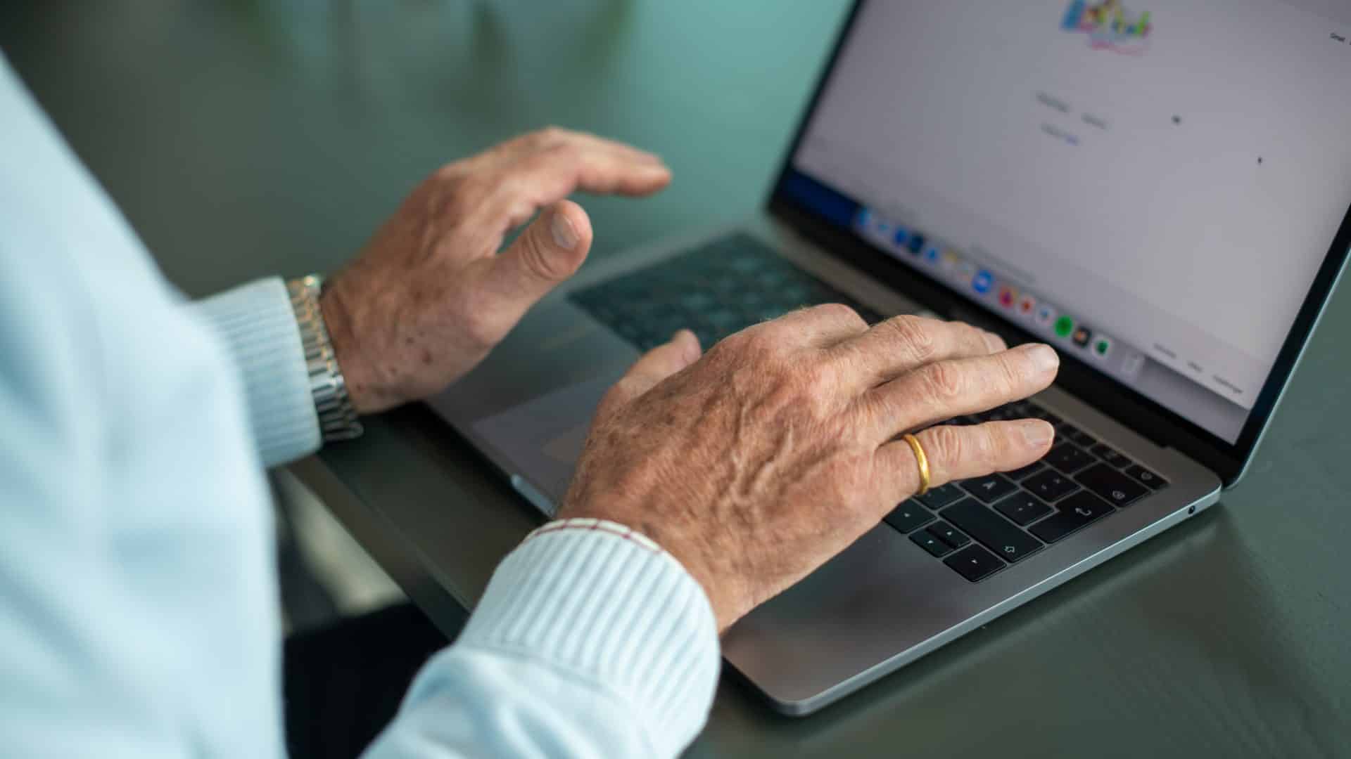Händerna på en äldre person som knappar på en dator.