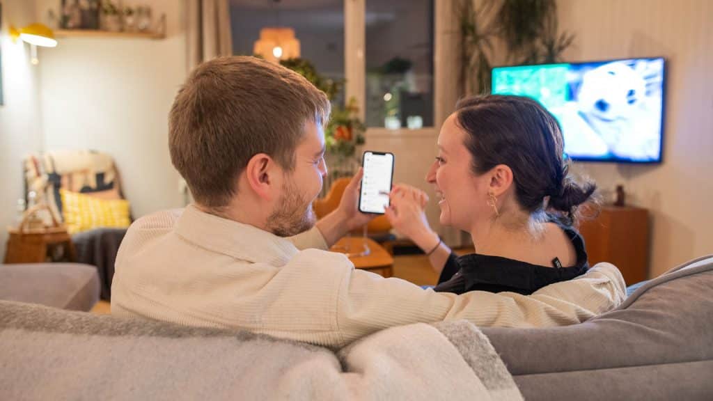 Par som sitter i soffan och tittar på mobilen.