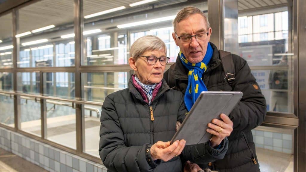 Ett äldre par står på en tunnelbanestation och tittar på något på en Ipad