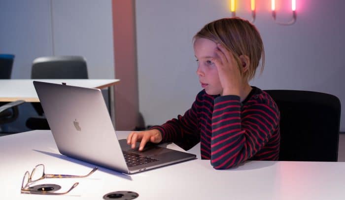 Ett barn sitter vid ett bord med en laptop framför sig.