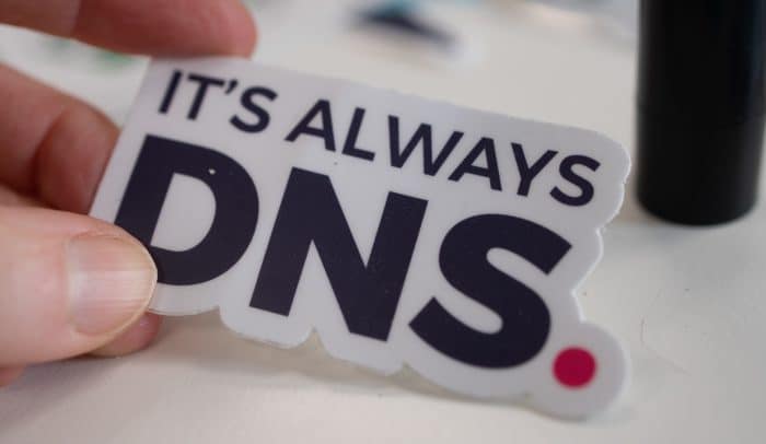 En hand som håller ett klistermärke som det står "it's always DNS" på.