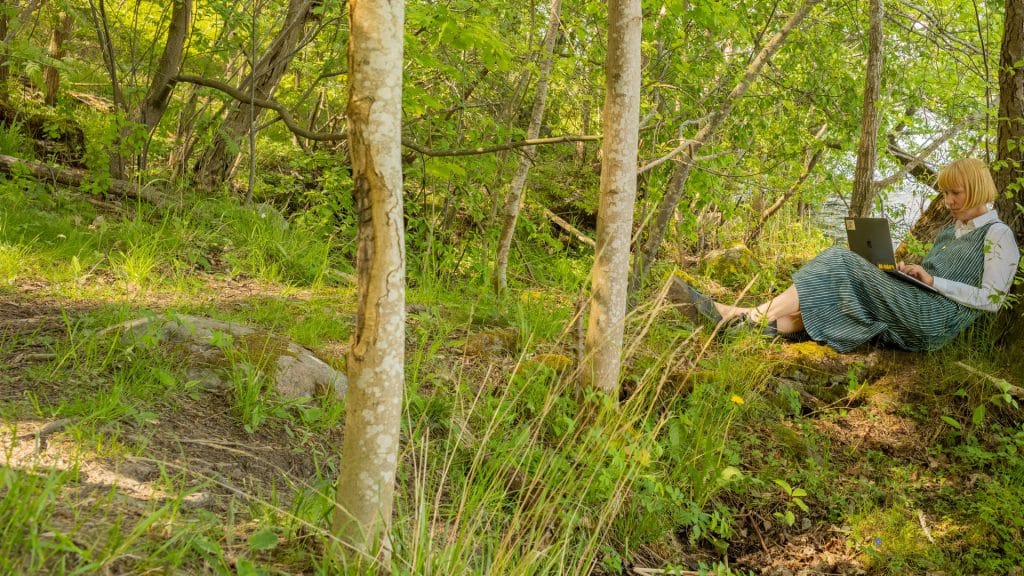 En kvinna sitter i skogen med sin laptop.