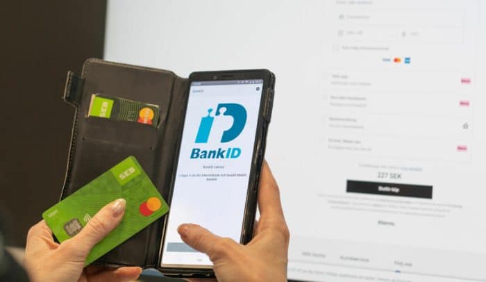Händer som håller i mobil med Bankid på skärmen och ett betalkort i andra handen.