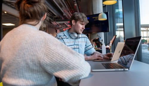 Två personer sitter på ett cafe med sina laptops framför sig.
