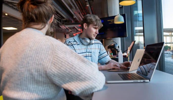 Två personer sitter på ett cafe med sina laptops framför sig.
