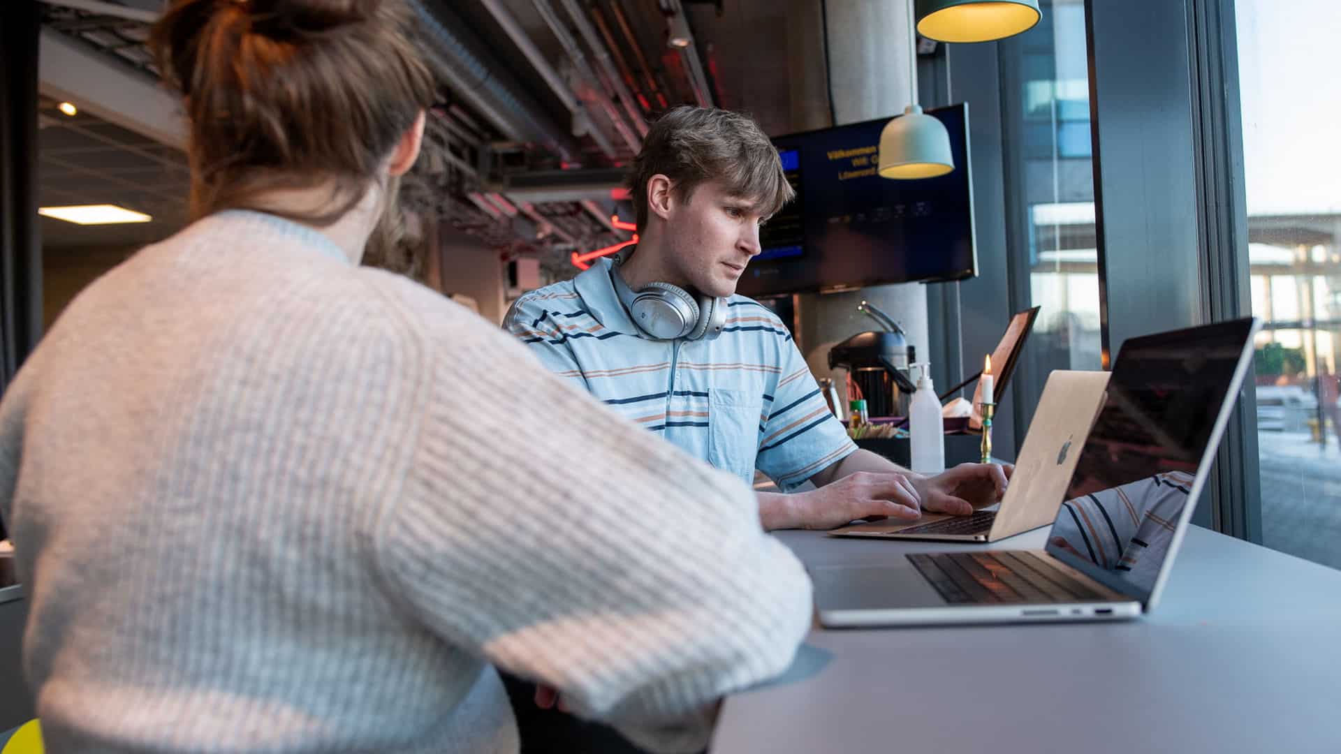 Två personer sitter på ett cafe med sina laptops framför sig.
