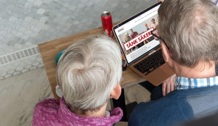 Två personer syns bakifrån, de tittar på en laptop-skärm med Tänk säkert-kampanjen.
