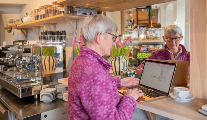 Äldre kvinna står med sin laptop på ett café.