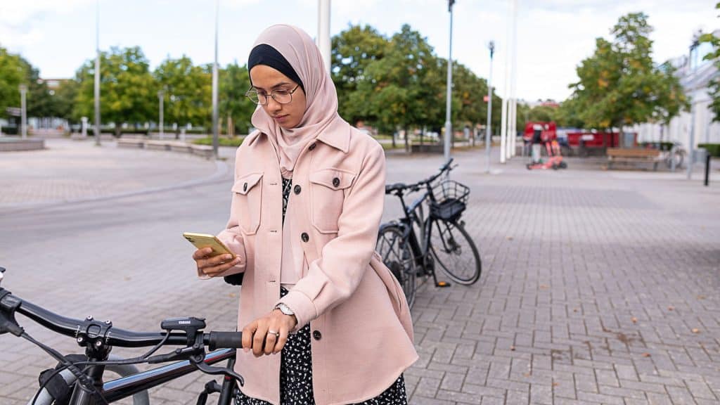 Många svenskar känner sig otrygga på nätet. Kvinna leder en cykel och använder mobiltelefon.