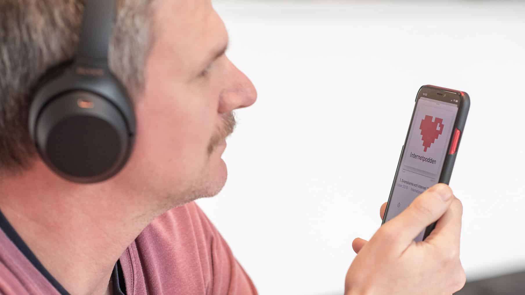 En man med hörlurar på sig håller i en mobil, på skärmen syns en podd.