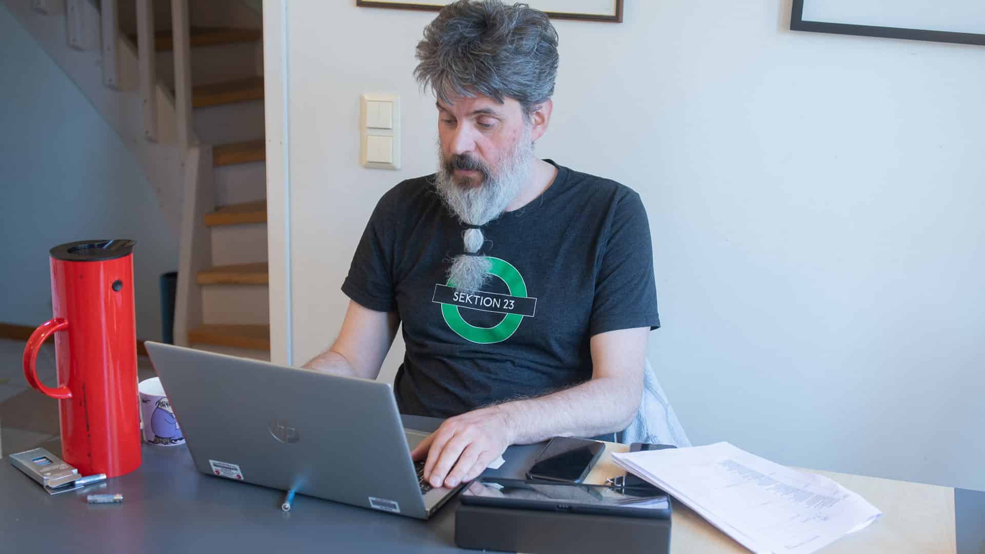 En man sitter vid en laptop, vid sidan står en röd termos.