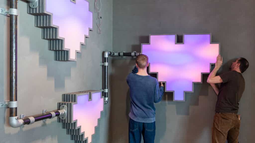 Två personer sätter upp hjärtan i neon på en vägg på Internetstiftelsens kontor.