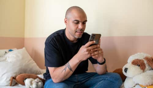 En man sitter i en säng och tittar på sin iphone.
