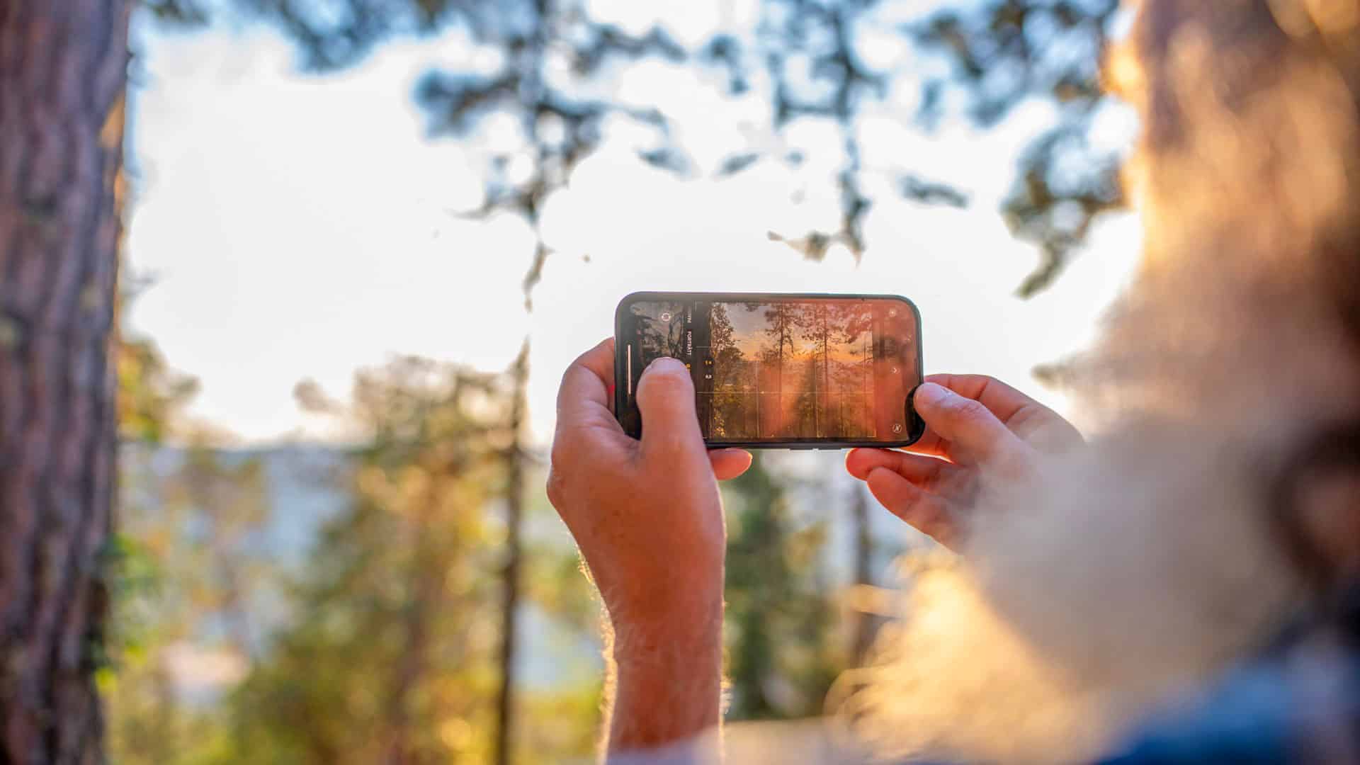 Person tar bild med mobilen ute i skogen.