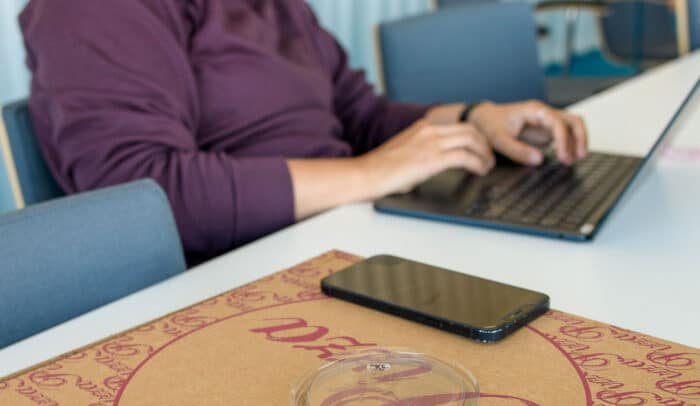 Händer på tangentbord på en laptop, bredvid ligger en mobil på en pizzakartong.