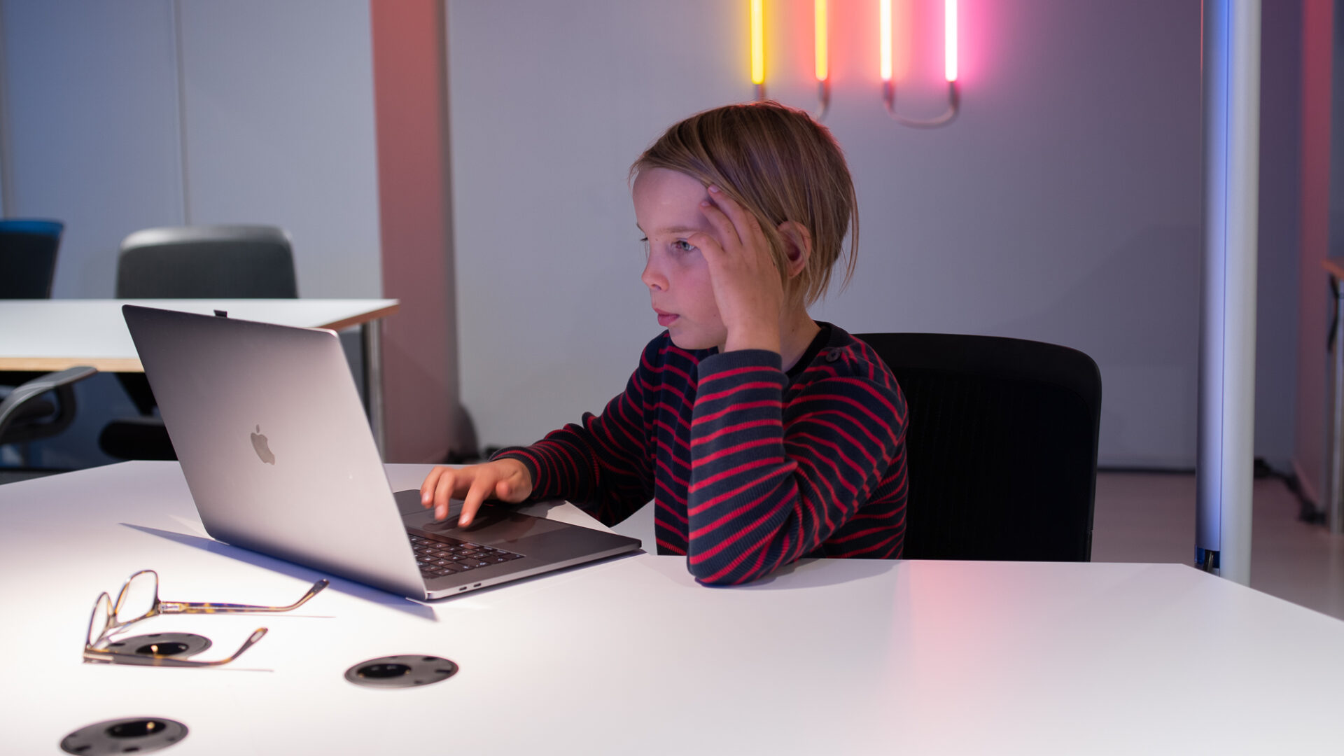 Ett barn sitter vid ett skrivbord framför en laptop.