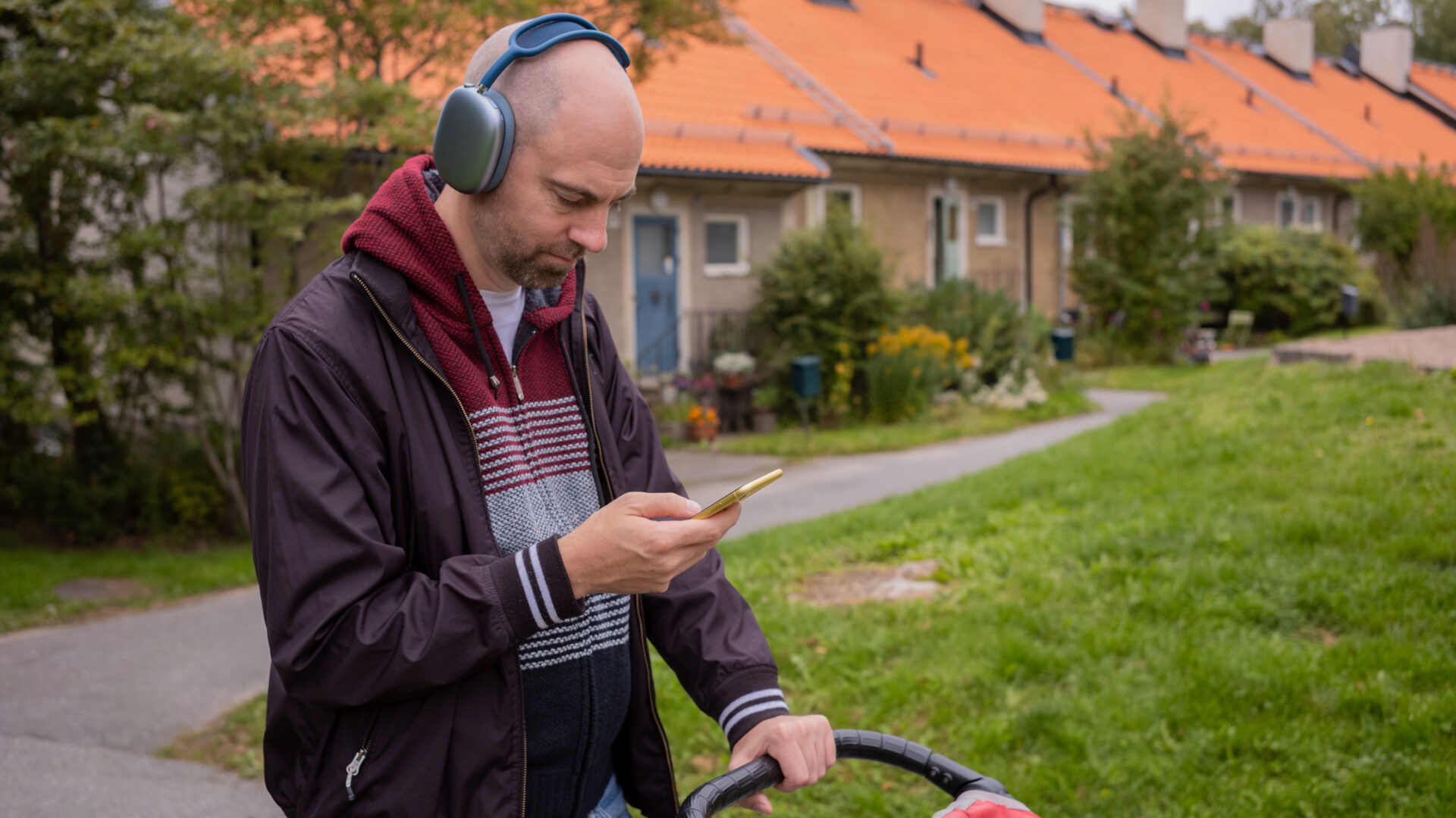 Man med hörlurar promenerar med barnvagn och lyssnar på podd via sin mobiltelefon.