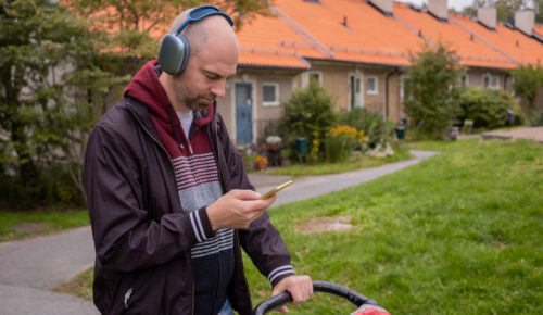 Man med hörlurar promenerar med barnvagn och lyssnar på podd via sin mobiltelefon.