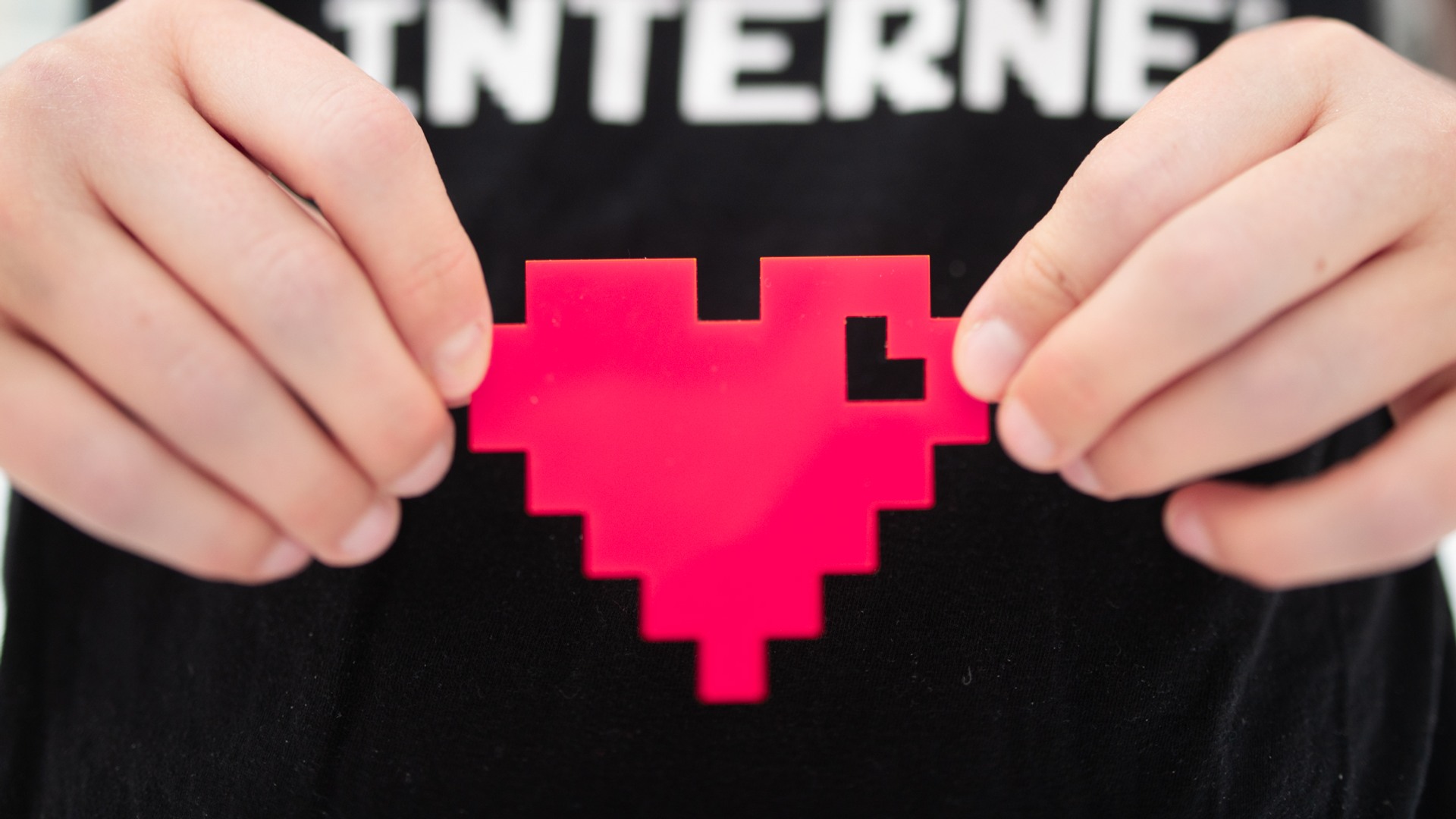 Två händer håller i ett rött pixel-hjärta.