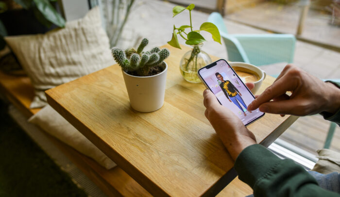 Händer håller en mobil, på skärmen syns en AI-person.