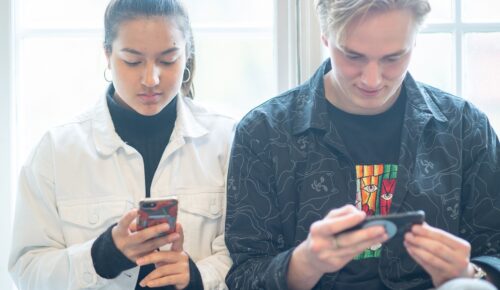 Två unga människor som tittar på sina mobiltelefoner.