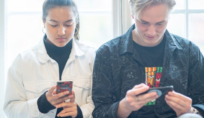 Två unga människor som tittar på sina mobiltelefoner.
