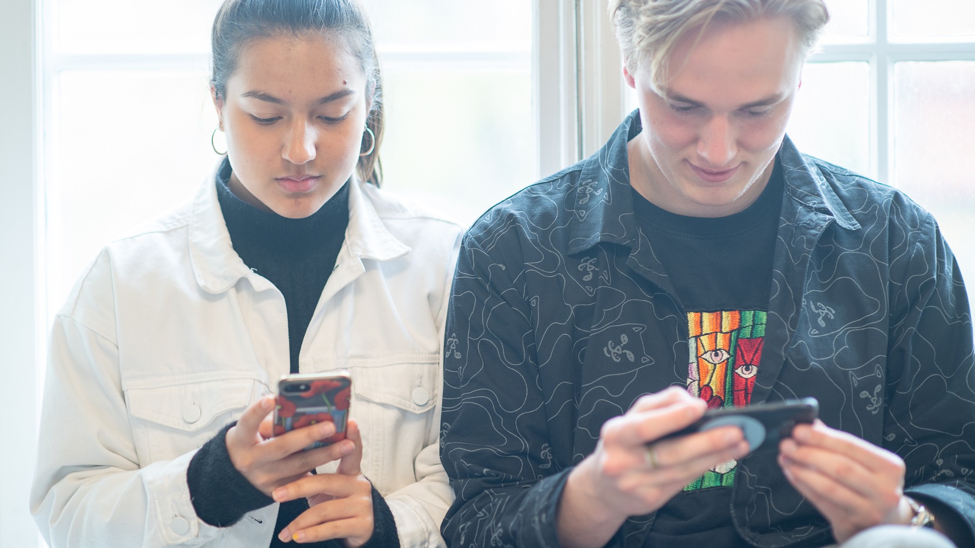Två unga människor som tittar på sina mobiltelefoner.
