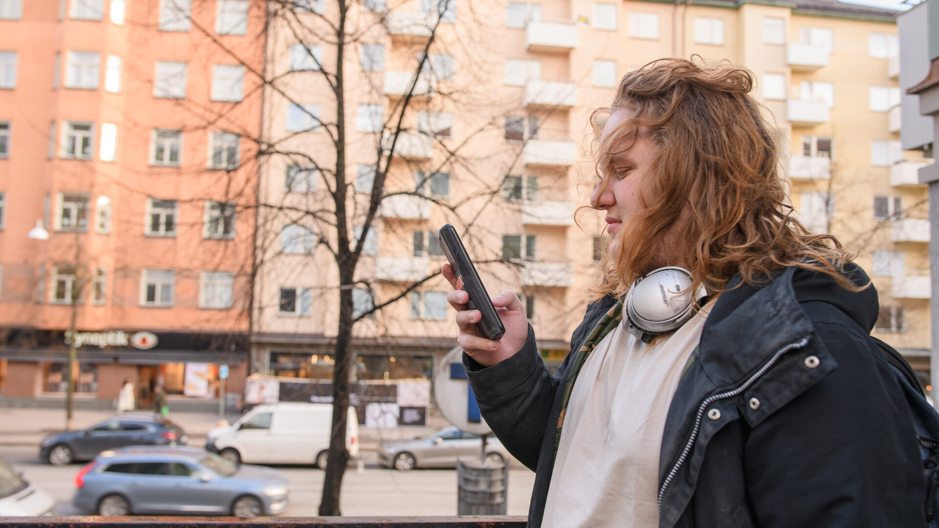 En ung man som står utomhus och tittar på sin mobil.