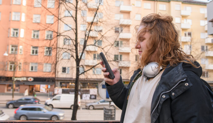 En ung man som står utomhus och tittar på sin mobil.