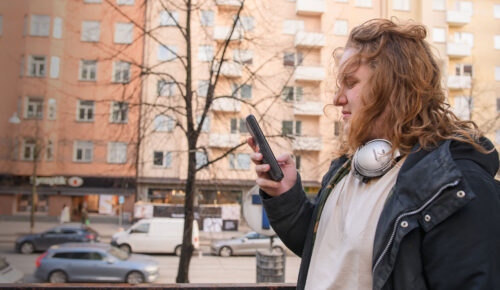 En ung man står utomhus och scrollar på sin mobil.